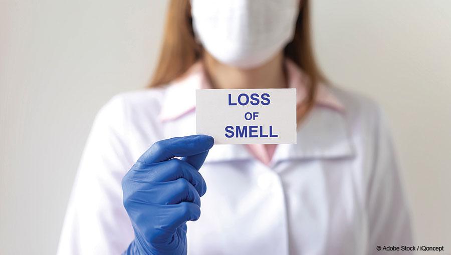 Woman in mask and gloved hand holding card that says, 'Loss of Smell'.