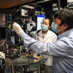 Nuo Li with a lab member adjusting a piece of scientific equipment.